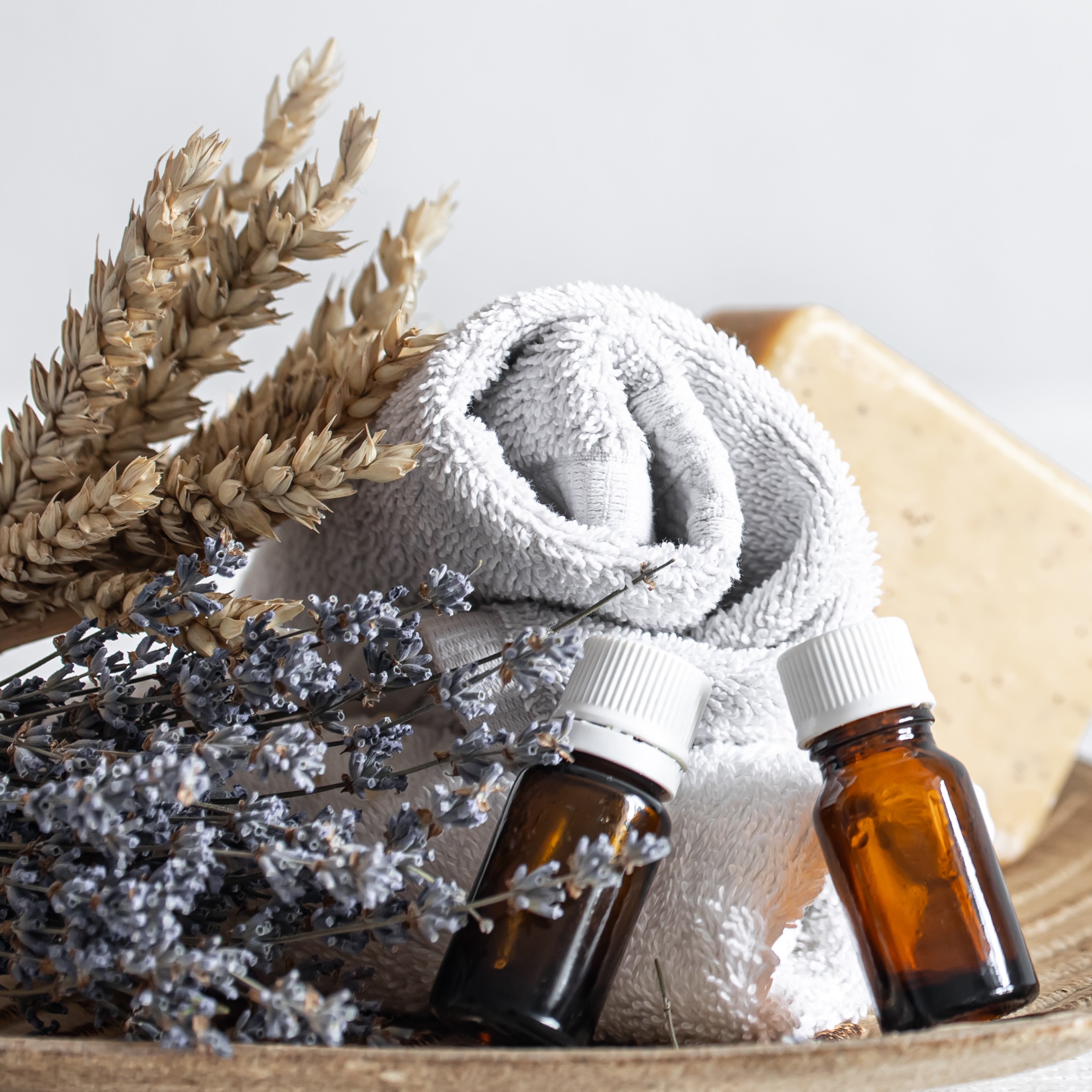 Two Bottles of UnlabledAromatherapy Oil Leaning Against a Rolled Up Towel with Sprigs of Lavender